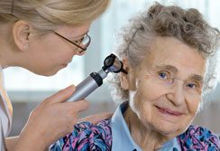 A woman is using an otoscope on the ear of an older person.