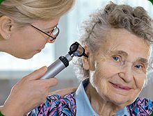 A woman is using an otoscope on the ear of an older person.